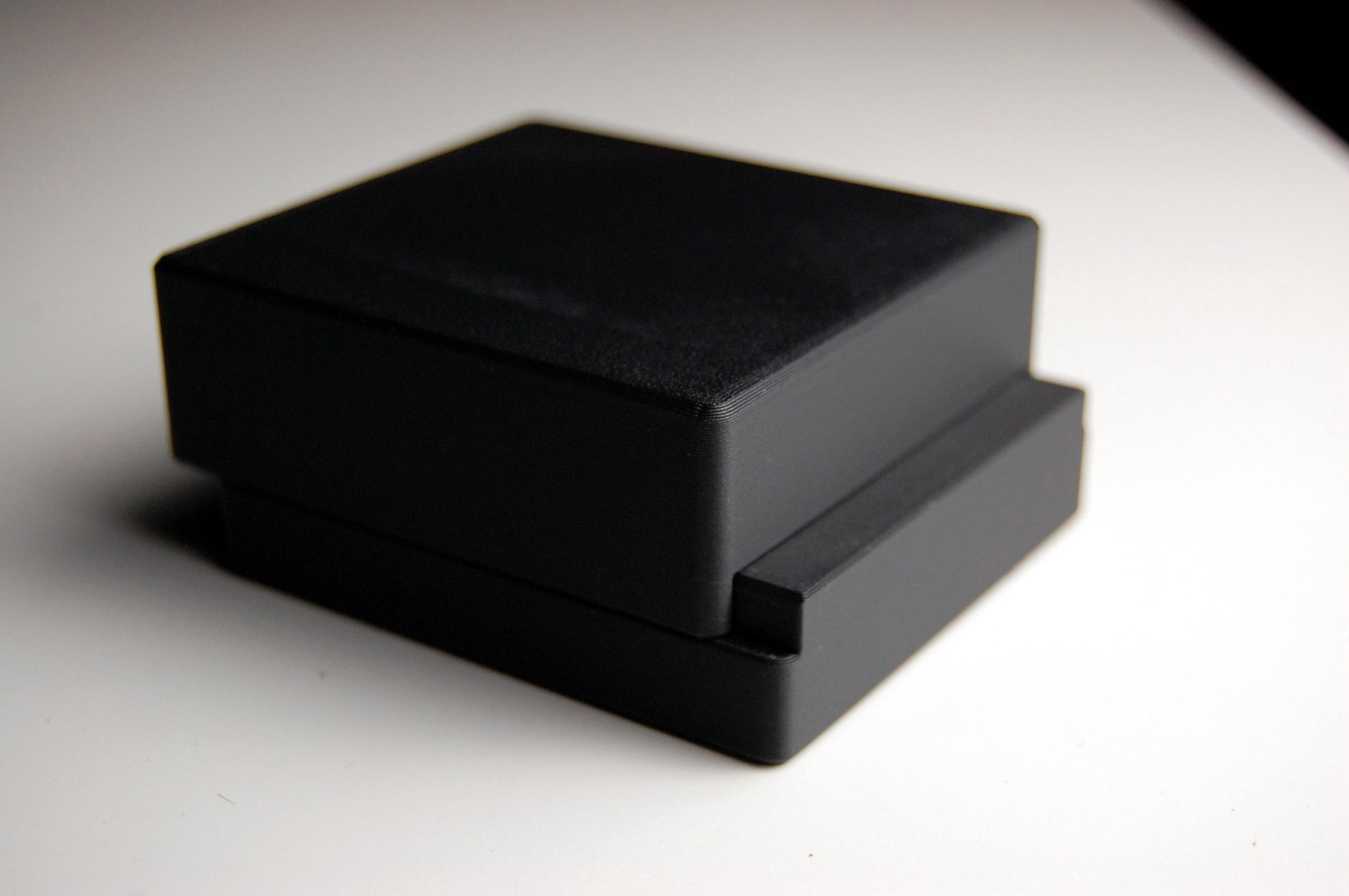 Black double edge razor blade storage box partially closed with 5 RK brand blade packs inside, resting on a white table with dark background.
