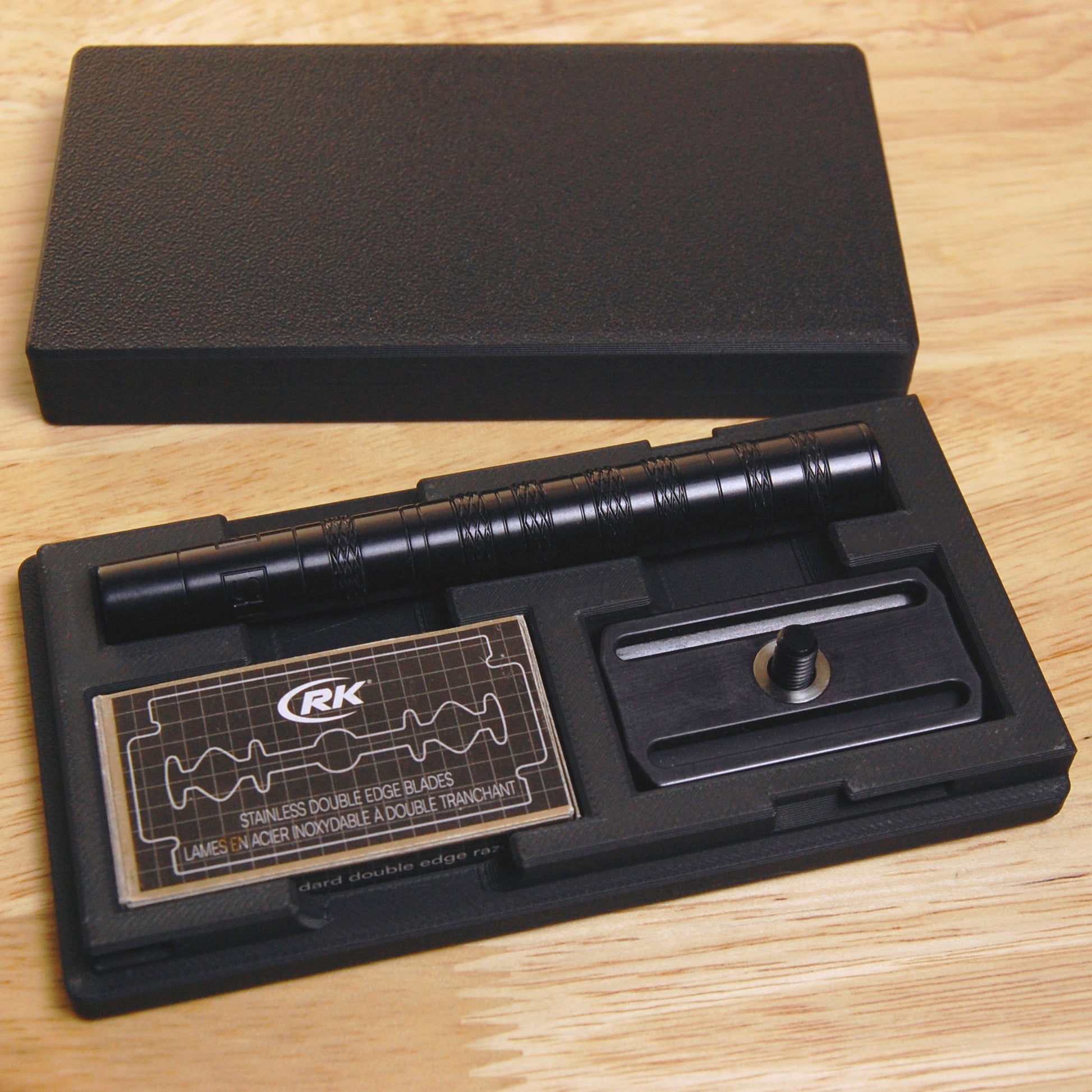 Sophisticated  black Henson razor case on a wooden background. The Henson razor and spare blades are in the case.