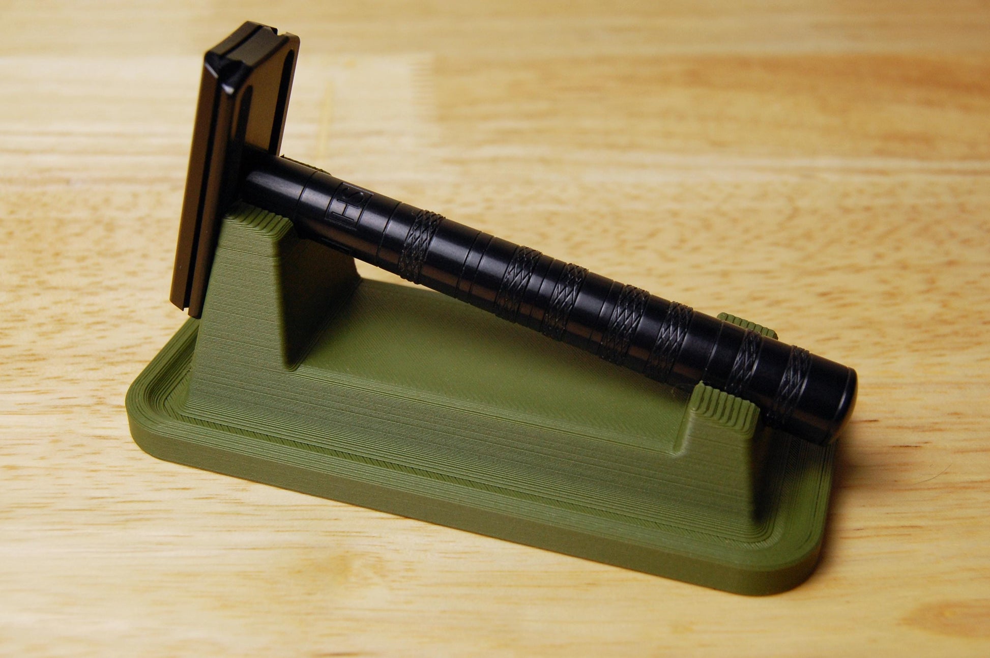 Stylish Henson Safety Razor Stand with drip tray in Olive displaying a black Henson Razor, safety razor. The stand is on a wooden butcher block table.