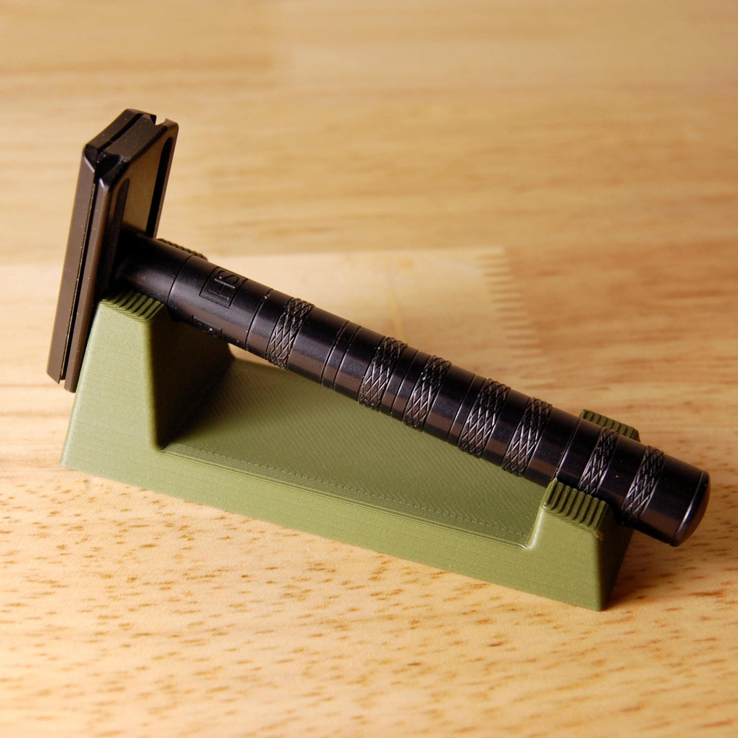 Stylish Henson Safety Razor Stand in Olive displaying a black Henson Razor, safety razor. The stand is on a wooden butcher block table.