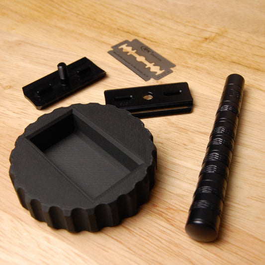 Black Henson Blade Installation and Removal tool on a wooden able.  A disassembled black Henson Razor is sitting around the tool.