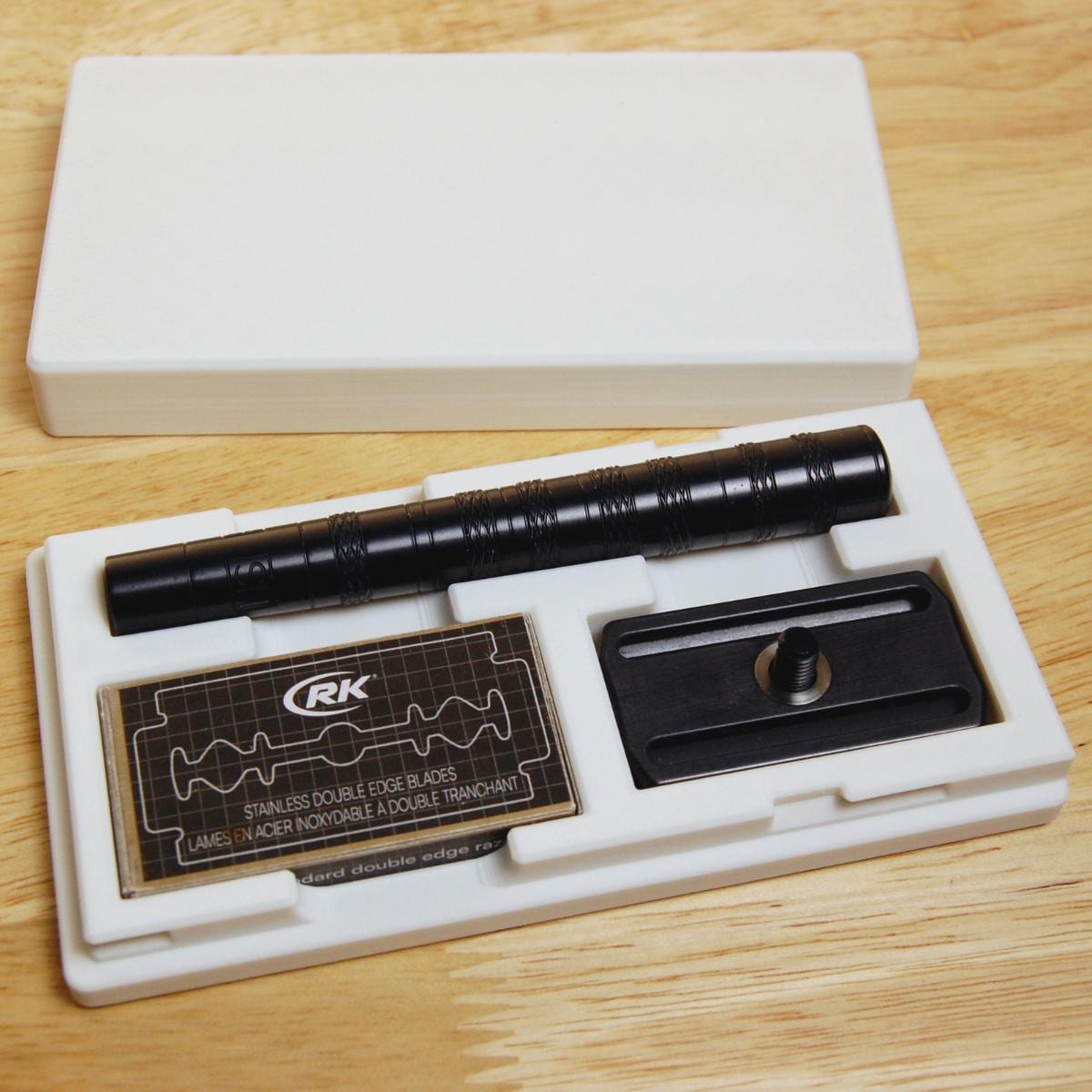 White Henson razor travel case on a wooden table with razor inside. Compact, protective case with built-in blade storage for AL13 and Ti22 razors. Perfect for travel, gym bags, and carry-ons.