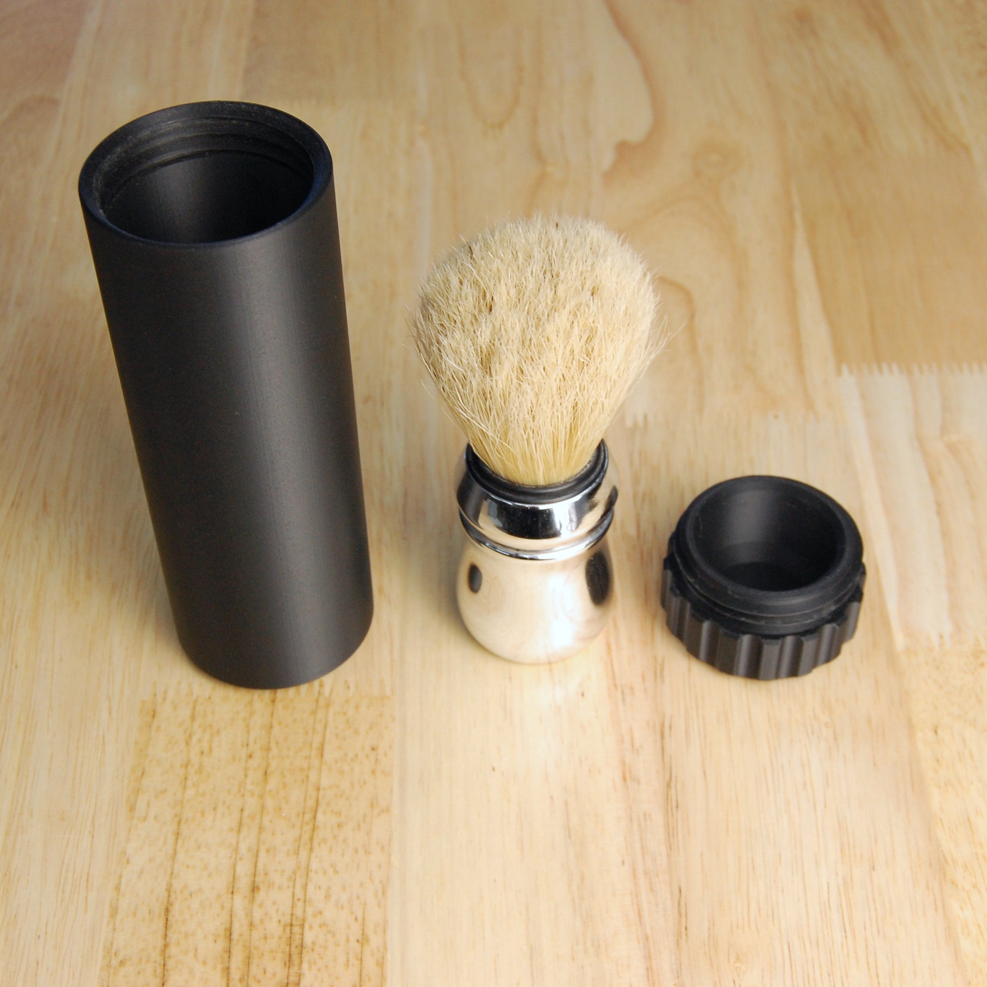 The capsule brush case unvented style in black next to a shaving brush on a wooden background.