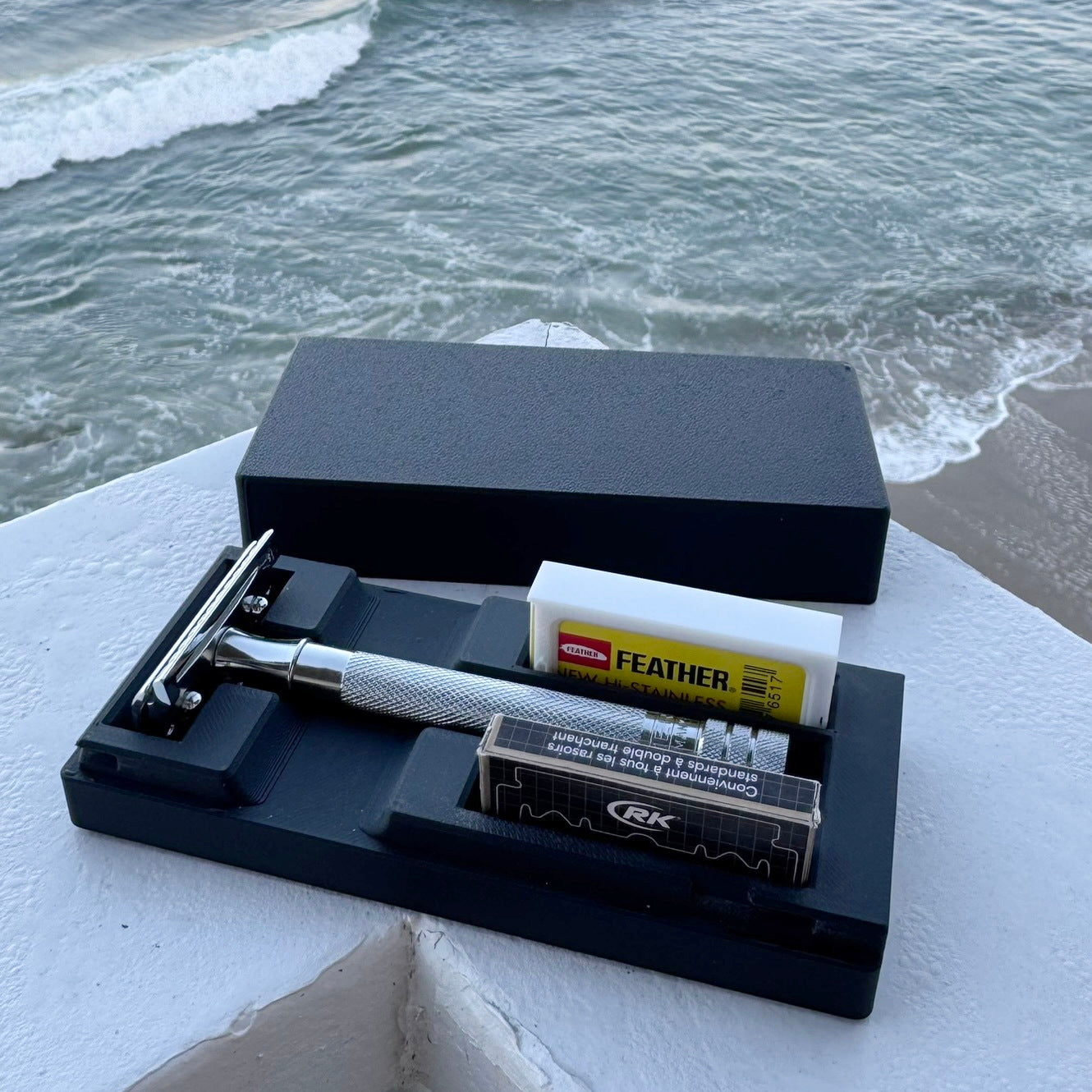 Black safety razor case in black sitting on a ledge by the ocean.