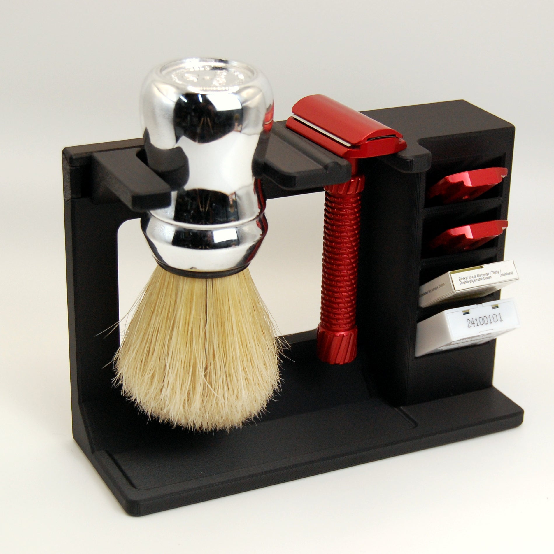 Chrome shaving brush in a black stand with a red razor, adjustment plates, and razor blades on a white background.