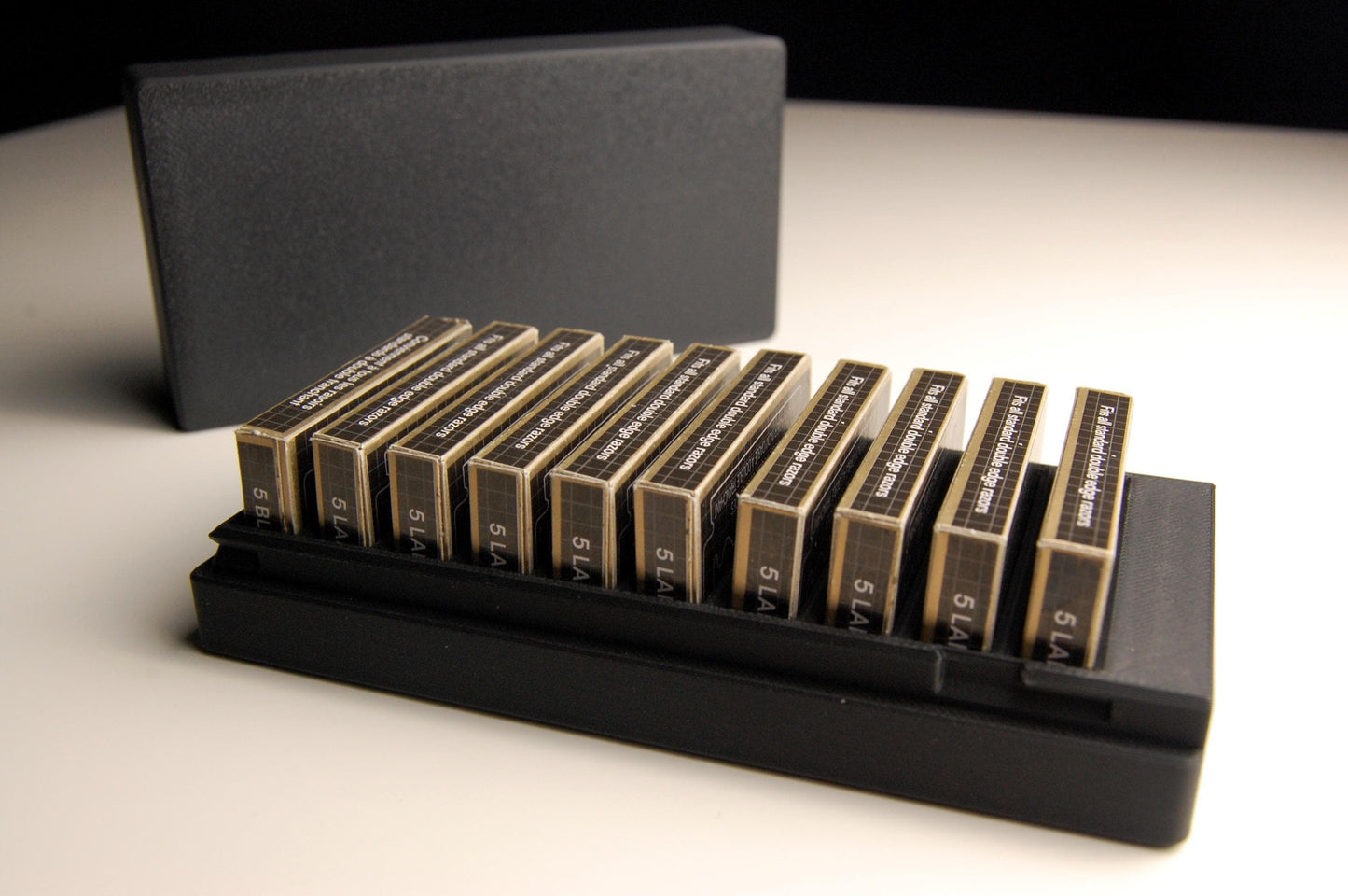 Black Double Edge Razor Blade box open on a white table. Close up view to show the details of the box.  This version holds 10 razor blade boxes.  10RK razor blades are in the box, other brands such as Astra or Gillette Feathers could also fit in the box.