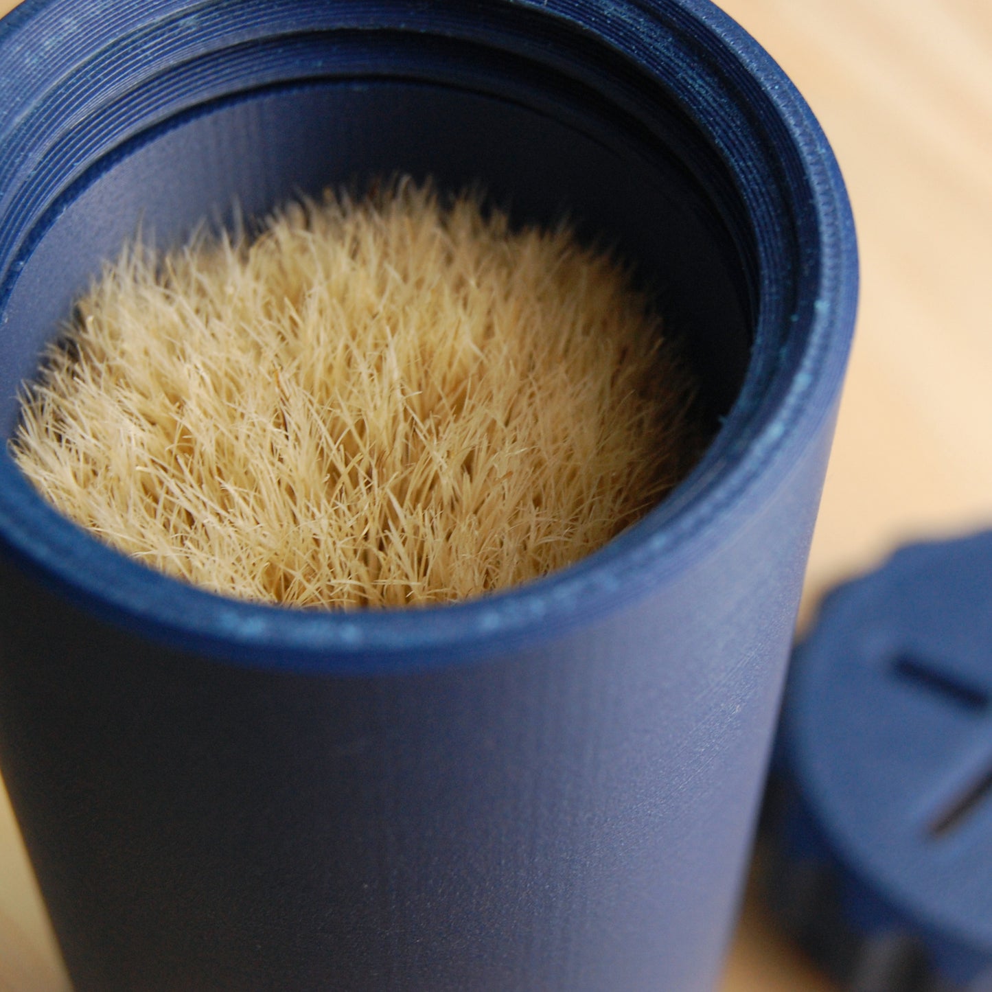 Navy blue capsule brush case on a wooden background.  The vented cap can be seen out of focus in the background.
