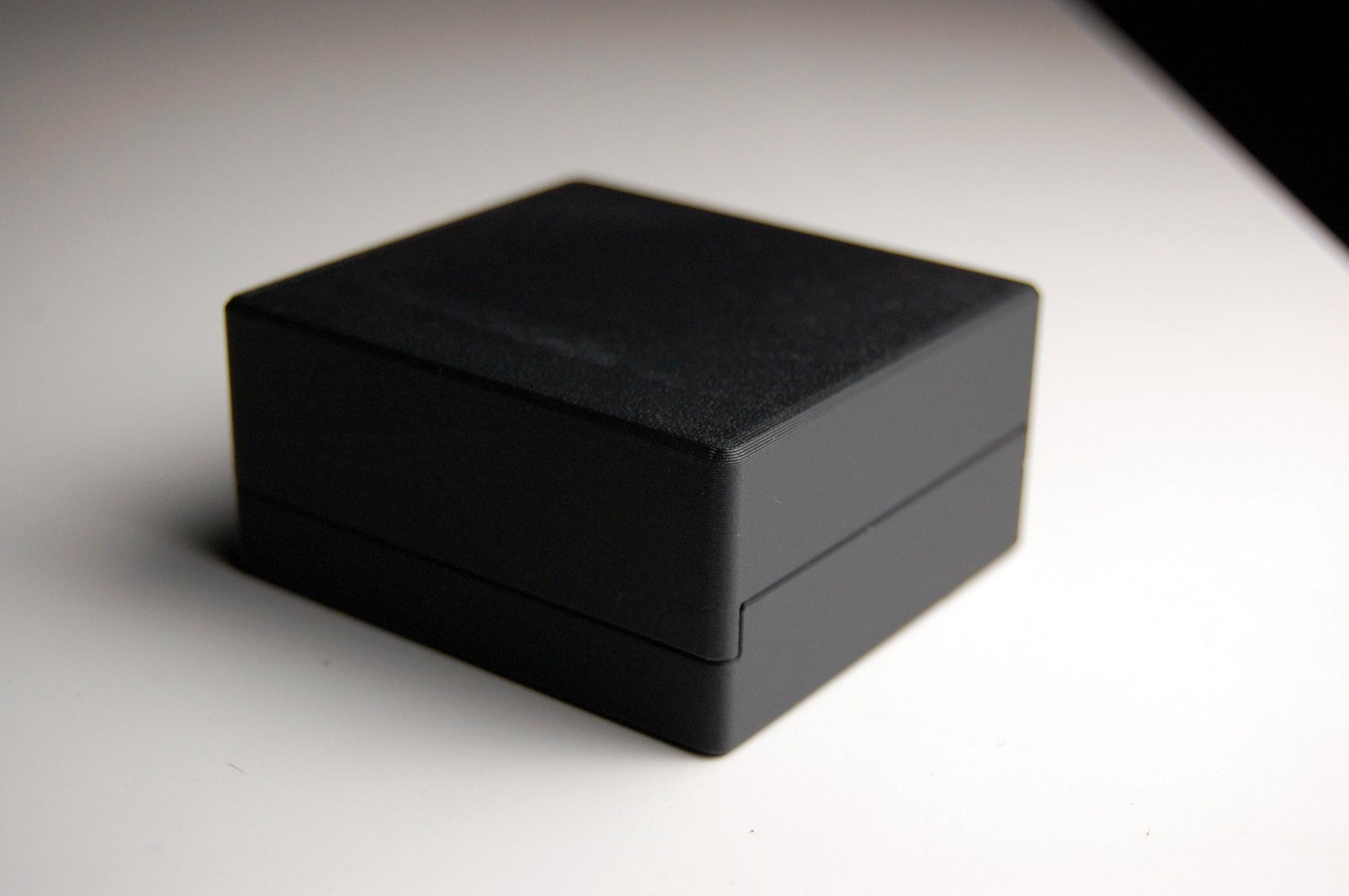 Closed black double edge razor blade box holding 5 RK blade packs, sitting on a white table with a dark background.