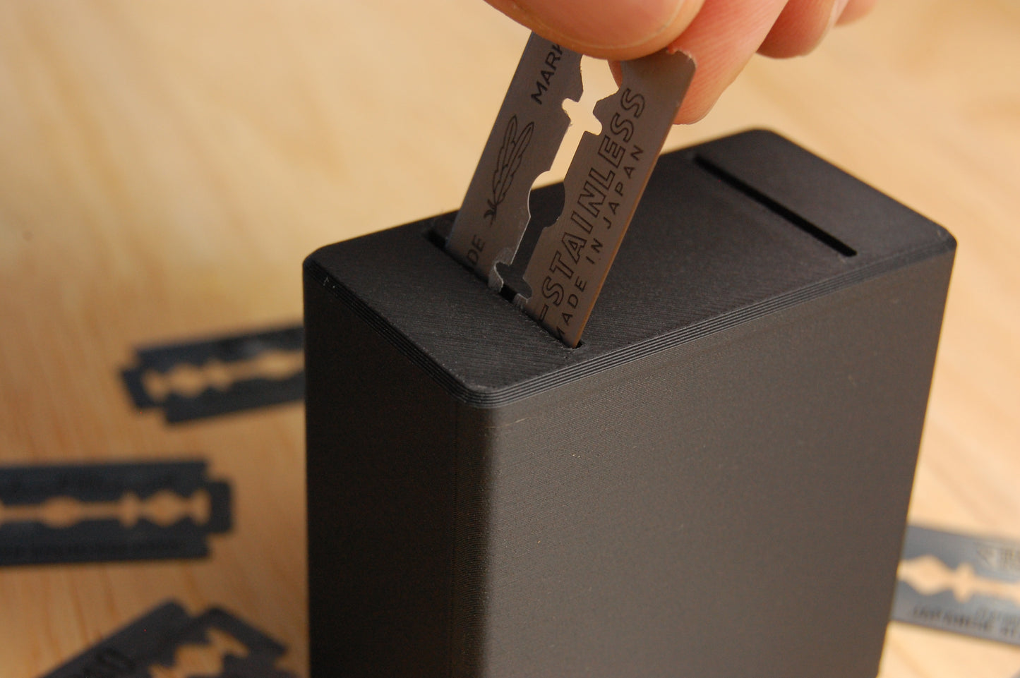 Closeup of a feather razor blade being inserted into the graveyard orbit blade bank.  Wooden background with razors blades strewn about can be seen.