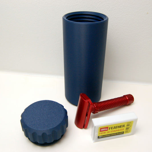 Navy blue capsule suborbital compact razor travel case.  Red razor and feather blade tuck pictured on a white countertop .