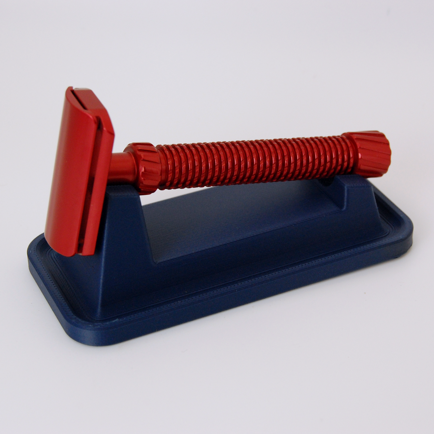 Universal razor stand with drip tray in navy blue on a white background. Pictured with a red Oliworks M3teorite razor.