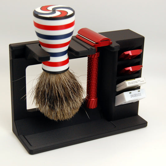 Shaving brush with red, white, and blue stripes in a black stand with a red razor, adjustment plates, and razor blades on a white background.