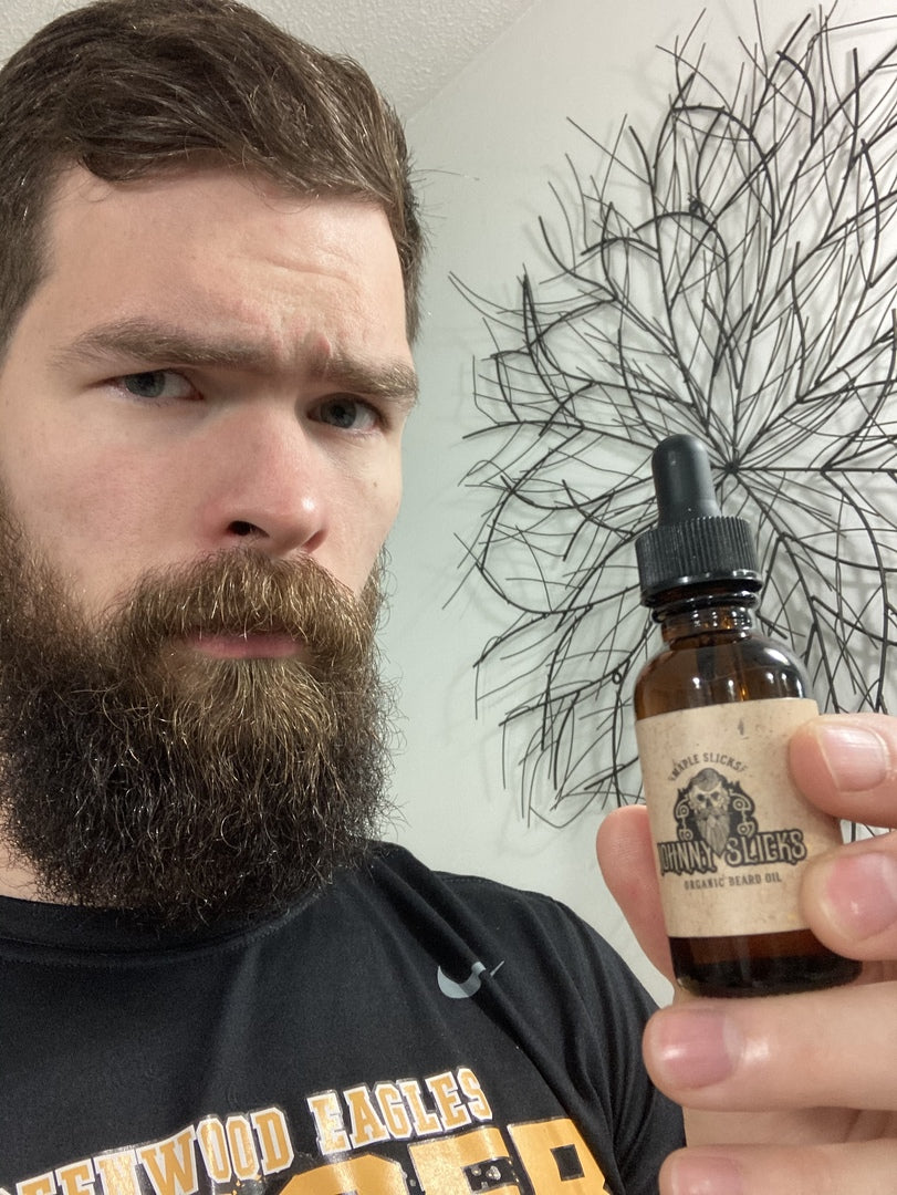 Bearded man holding amber dropper bottle of Johnny Slicks Maple Slicks Organic Beard Oil with kraft label