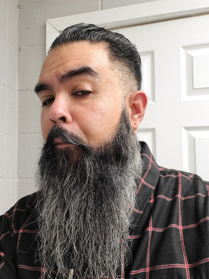 Man with long full beard transitioning from dark to gray, styled and well-groomed, wearing a black plaid shirt