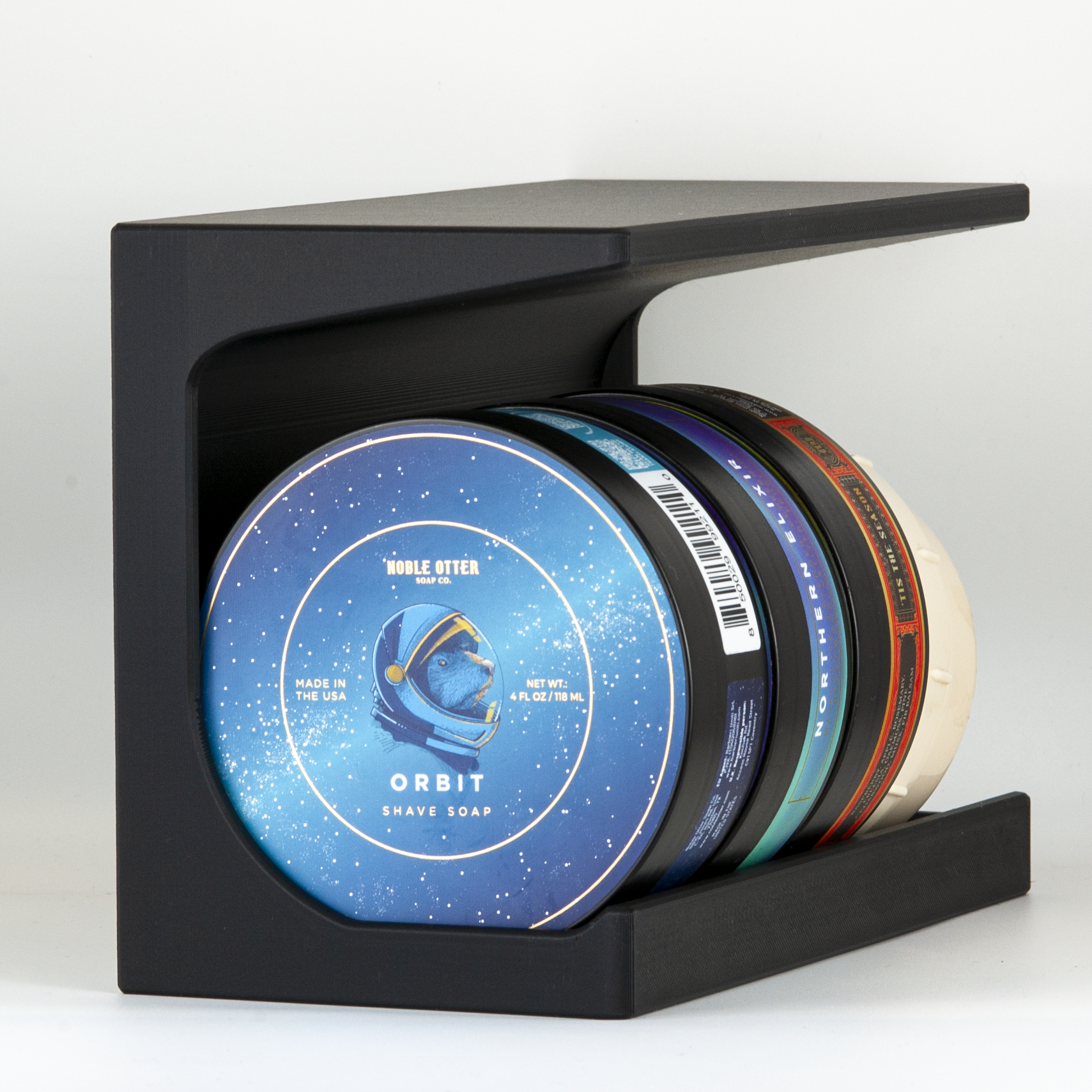 Black soap stand with a variety of Noble Otter shaving soaps on a white background.