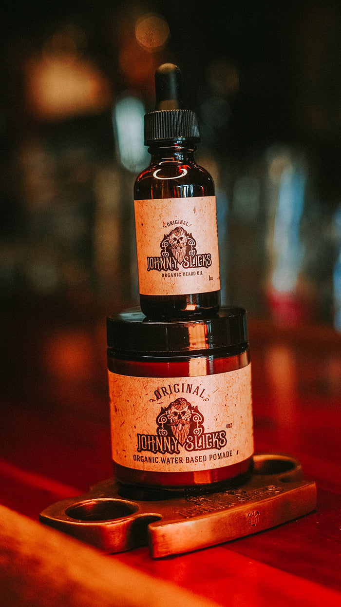 Johnny Slicks Original Organic Beard Oil dropper bottle and Organic Water Based Pomade jar on a brass knuckle display stand