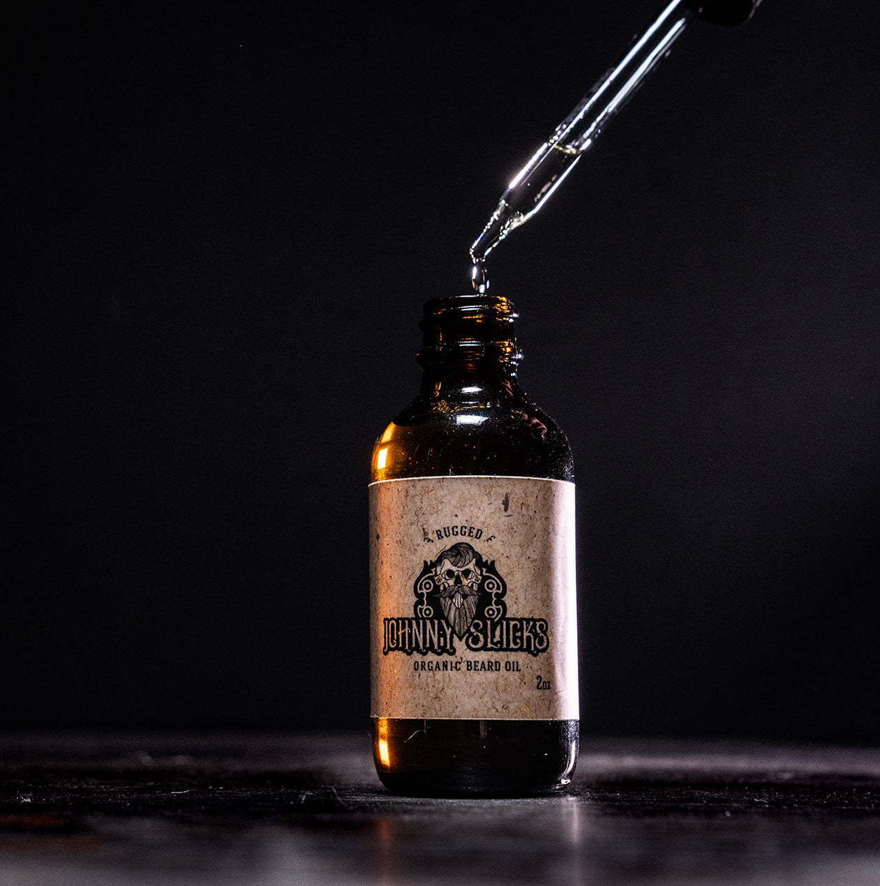 Johnny Slicks Rugged Organic Beard Oil 2oz amber glass bottle with dropper dispensing oil, skull logo on label