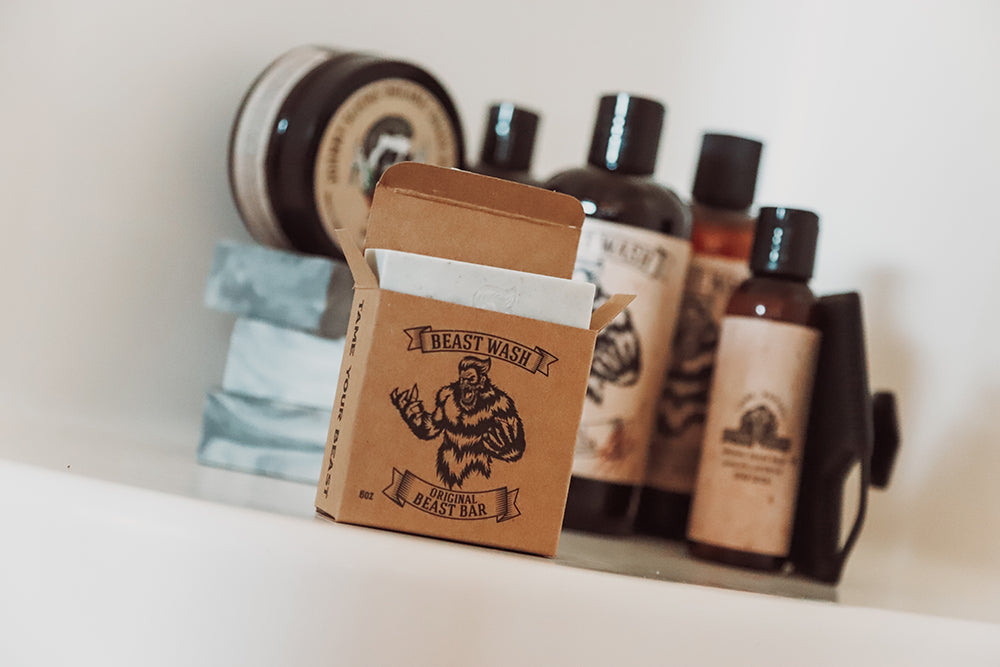 Beast Wash Original Beast Bar soap in open brown kraft box on shelf with assorted Tame Your Beast grooming bottles and tins