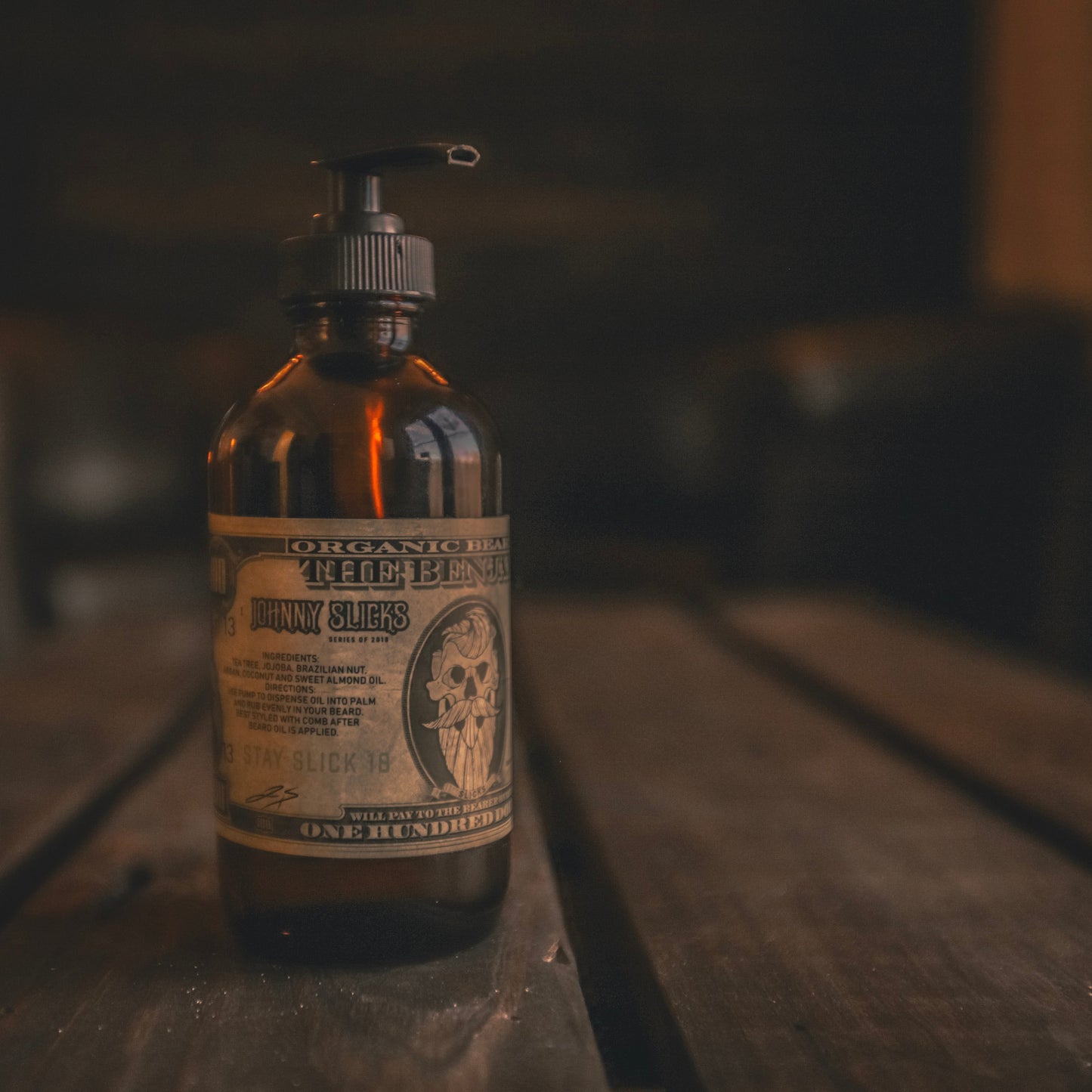 Johnny Slicks Organic Beard Oil "The Benjamin" in amber glass pump bottle on dark wooden surface