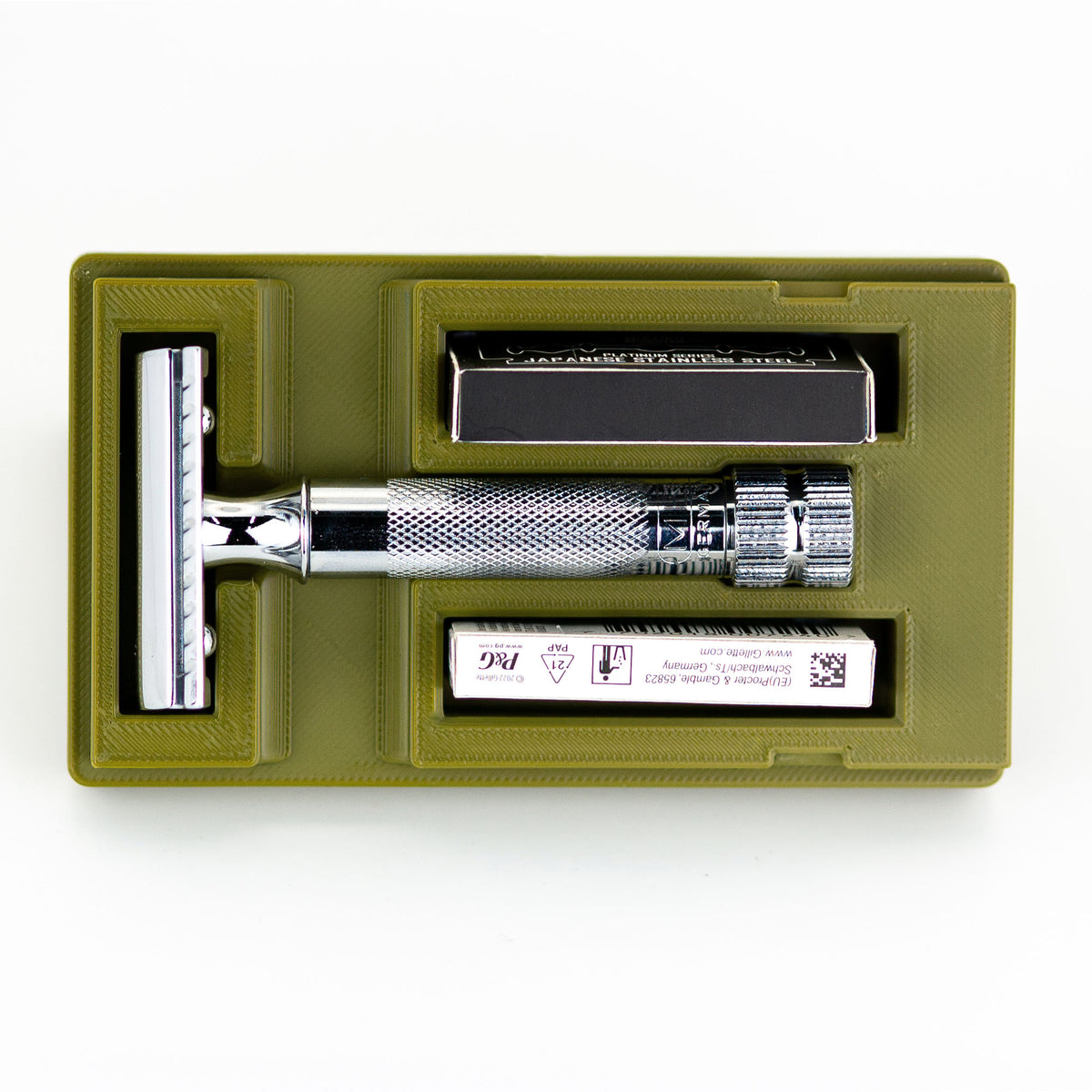 Open army green Merkur 34C safety razor travel case with chrome butterfly-style razor handle, box of Astra blades, and chrome baseplate