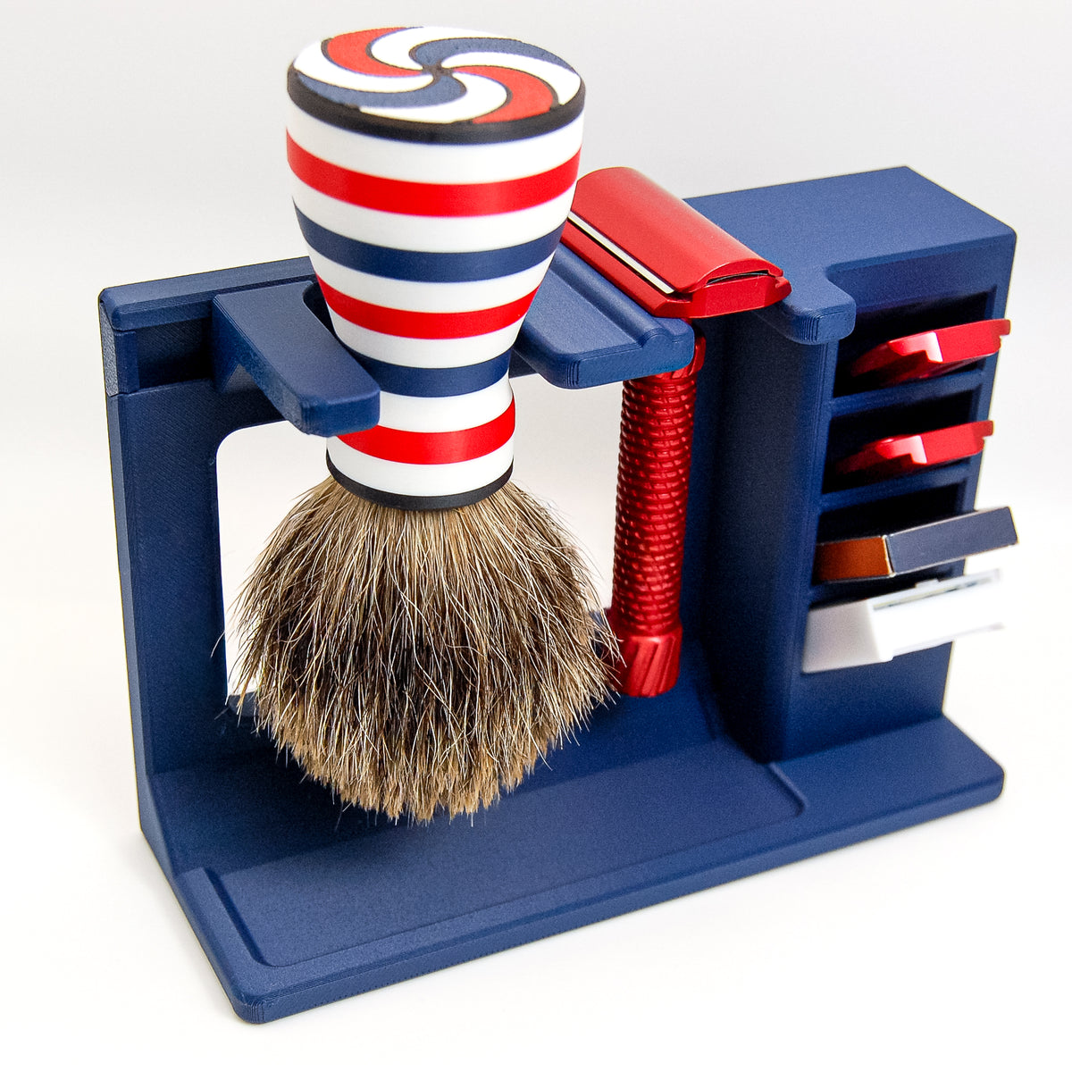Navy blue stand holding a red-white-blue striped badger shaving brush and red adjustable safety razor with blade storage