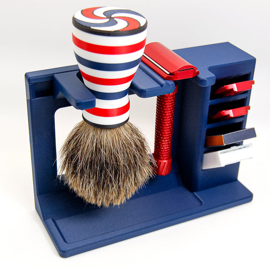 Navy blue stand holding a red-white-blue striped badger shaving brush and red adjustable safety razor with blade storage
