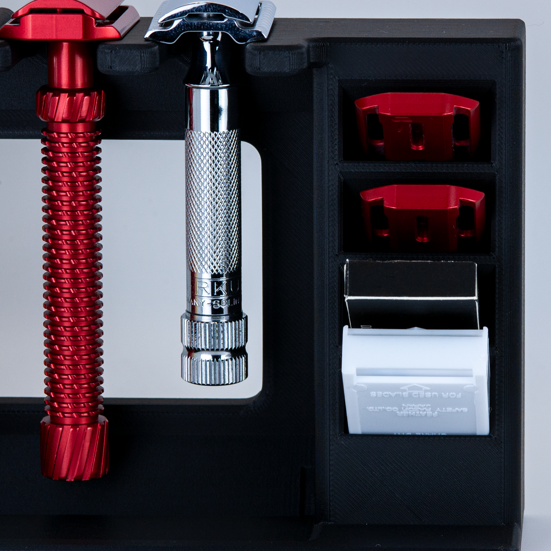 Black Mission control two razor countertop shave organizer on a white background.  A red Oliworks razor and chrome Merkur razor are hanging in the stand. 