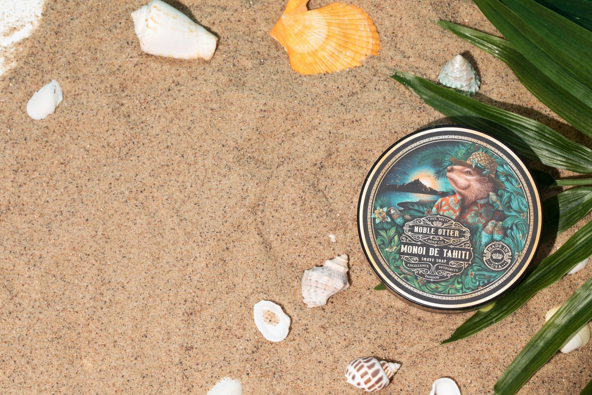Noble Otter have soap container with a tropical design on a sandy background with shells and leaves