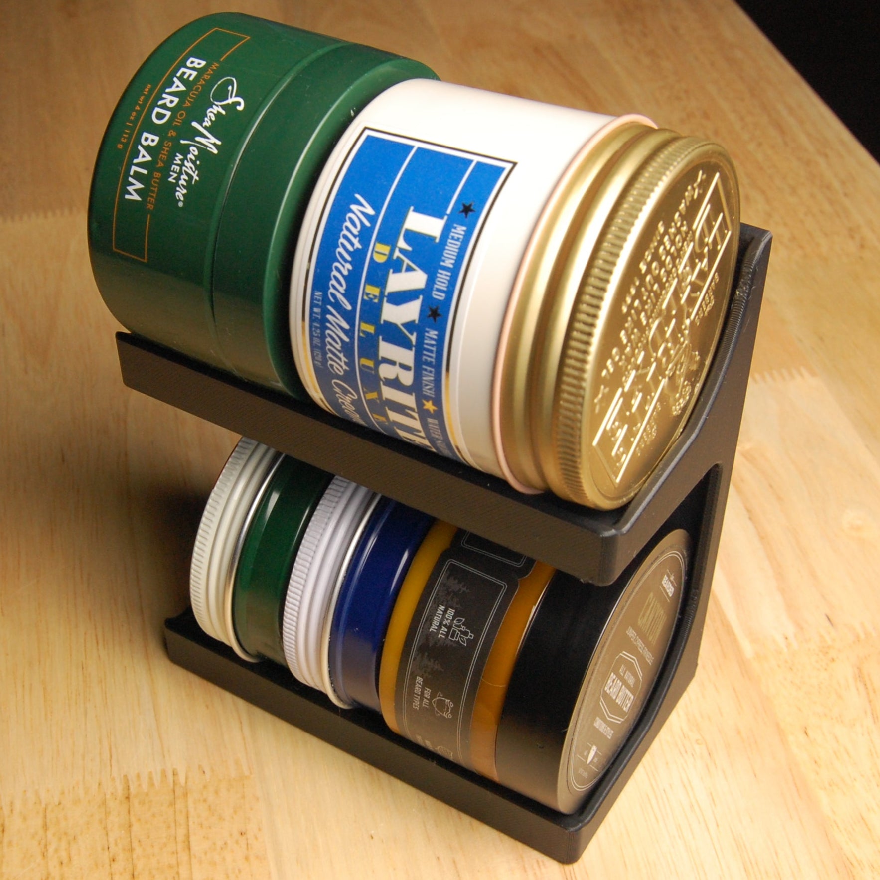 Collection of pomades and beard balms on a stylish black stand, sitting on a wooden table.