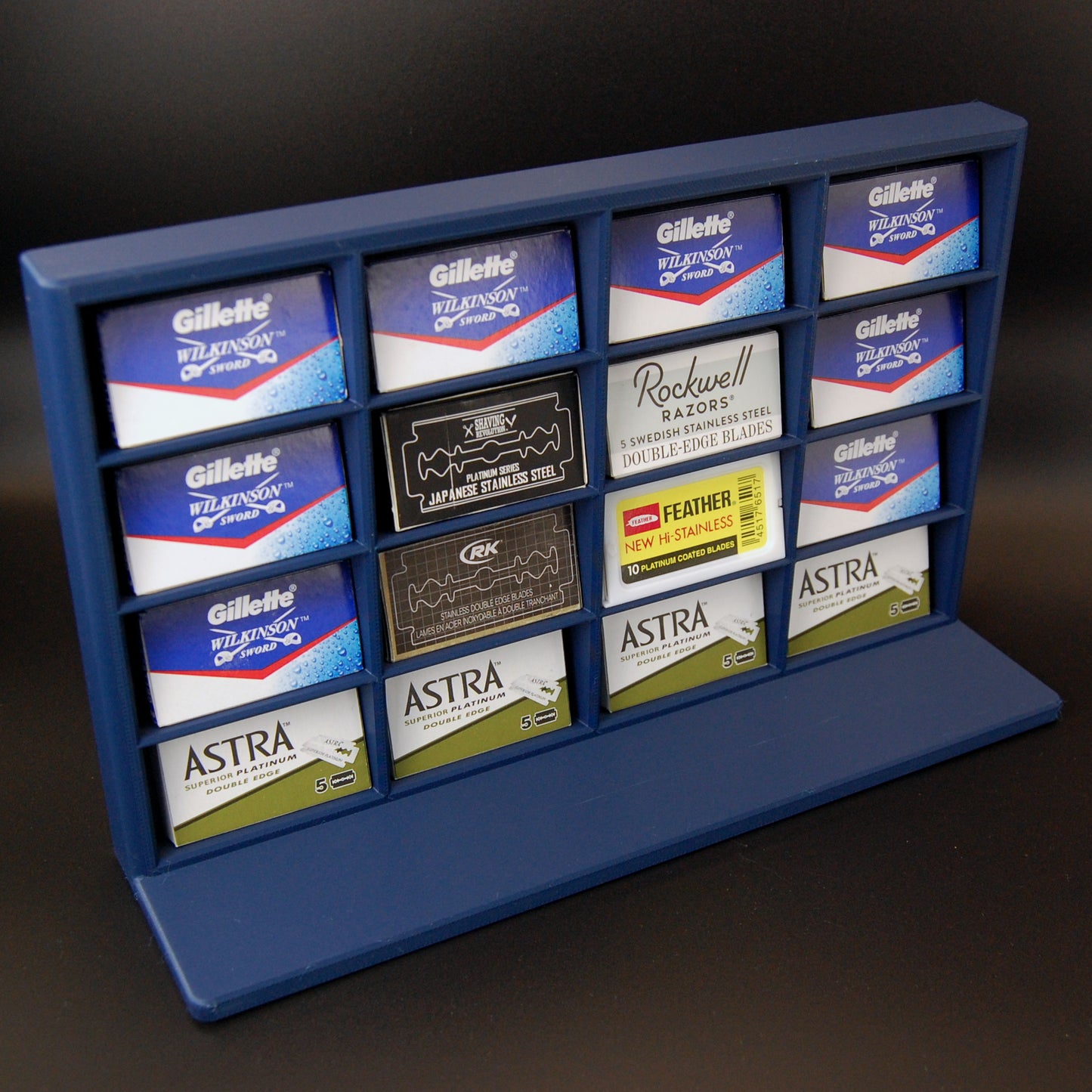 Various razor blade tucks stored in a navy blue razor blade display stand on a black background. Astra, Gillette, Shaving Revolution, RK, Rockwell and Feather blades are stored.