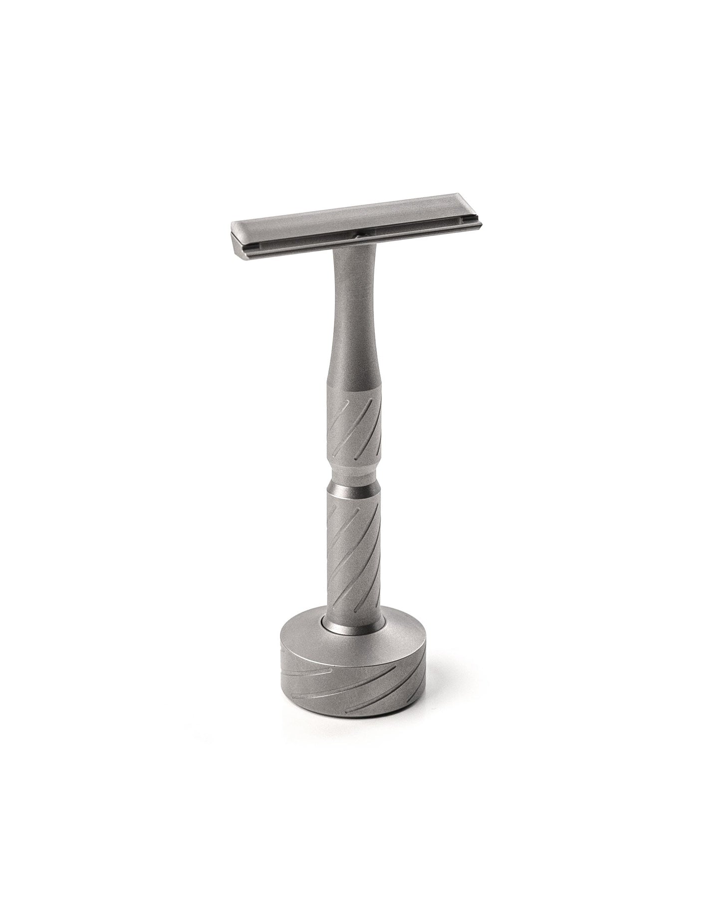 Matte titanium double-edge safety razor with diagonal-grooved handle, standing upright on a matching round titanium stand
