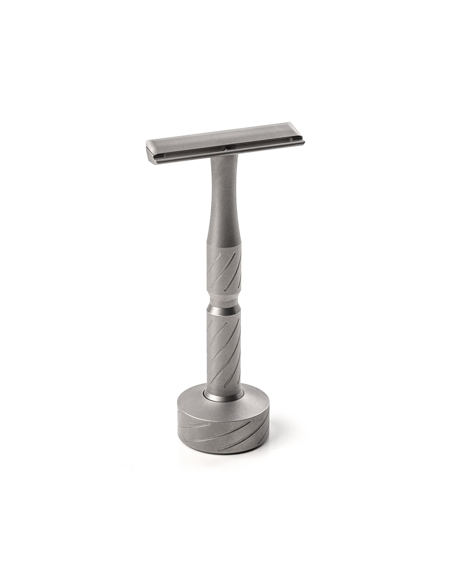 Matte titanium double-edge safety razor with diagonal-grooved handle, standing upright on a matching round titanium stand