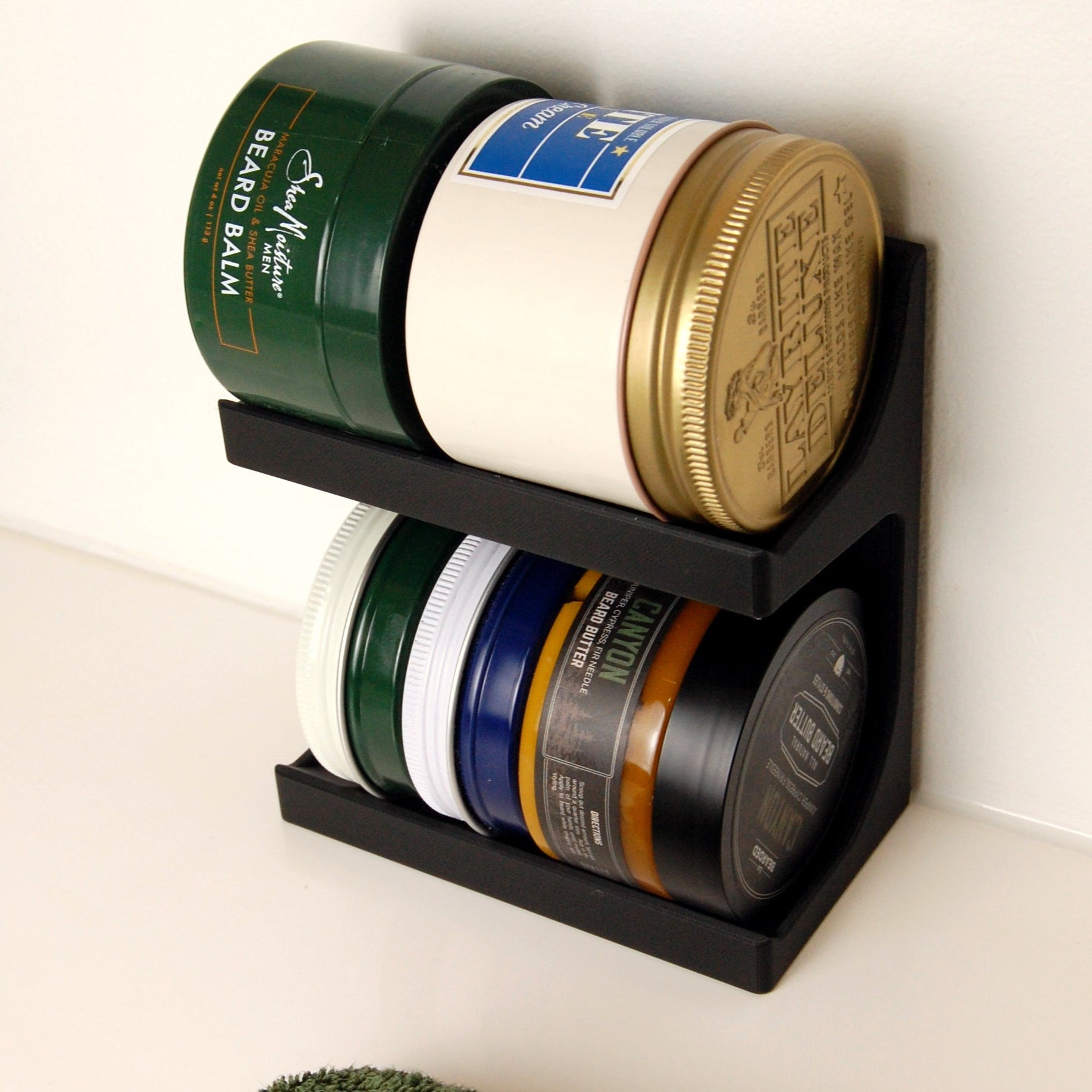 Black wall-mounted shelf holding various containers of beard balm and related products.