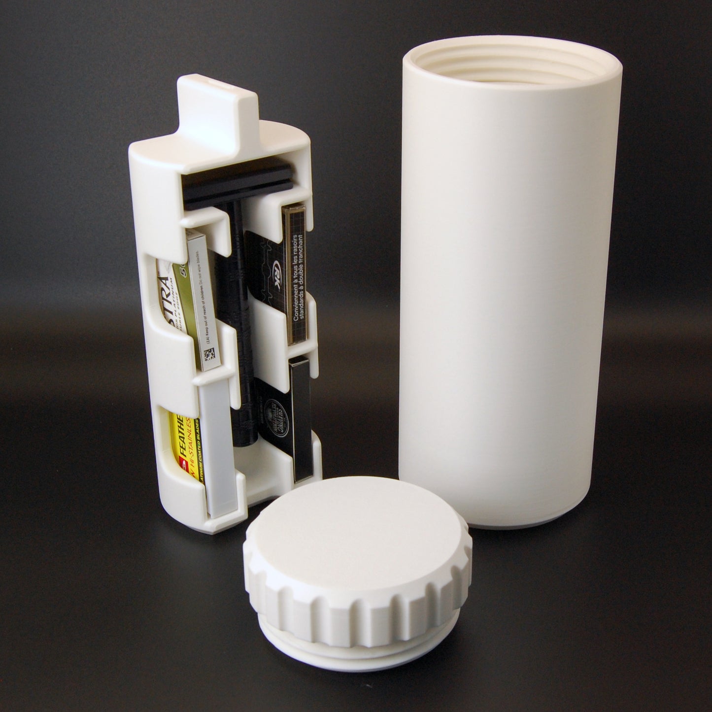 White capsule travel case with a black Henson AL13 safety razor and razor blades sitting on a black background