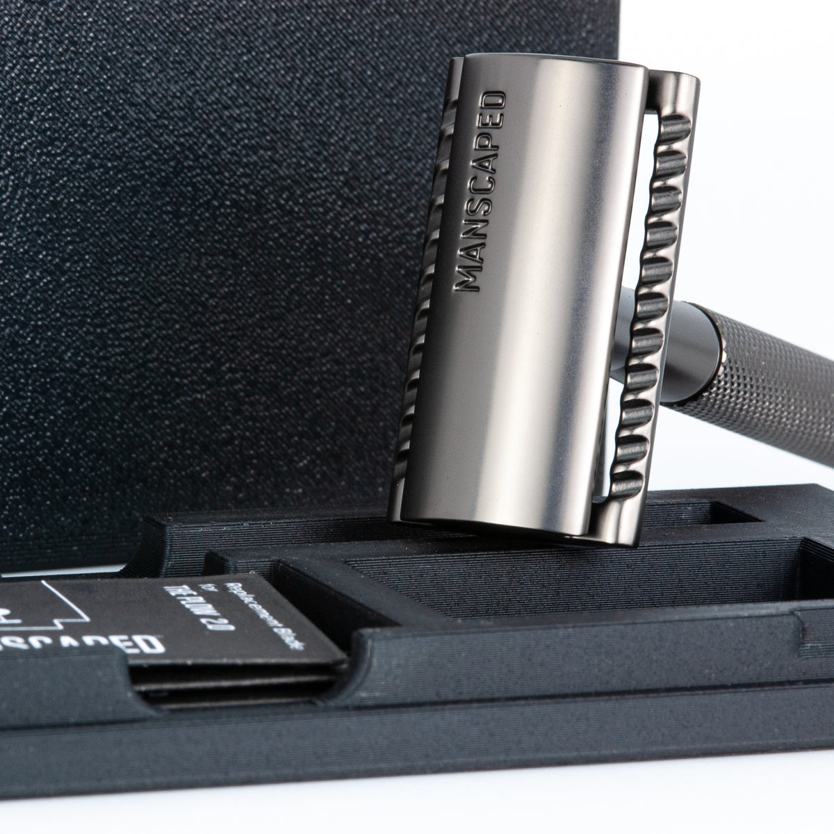 Close-up of the Manscaped Plow 2.0 razor head engraved with the Manscaped logo, standing upright in front of its travel case
