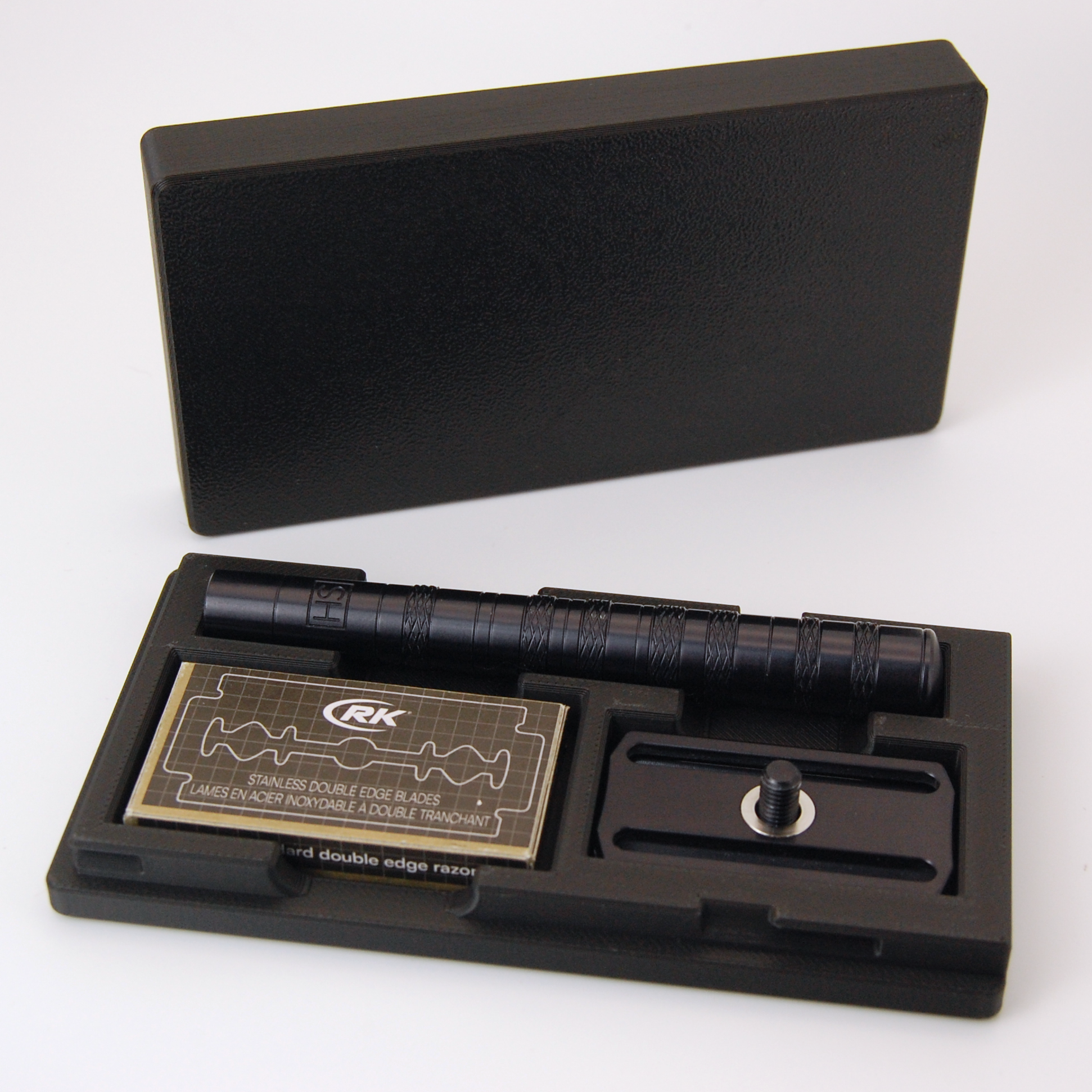 Henson case in black on a white background.  Black Henson razor is stored inside with a blade tuck of RKrazor blades.