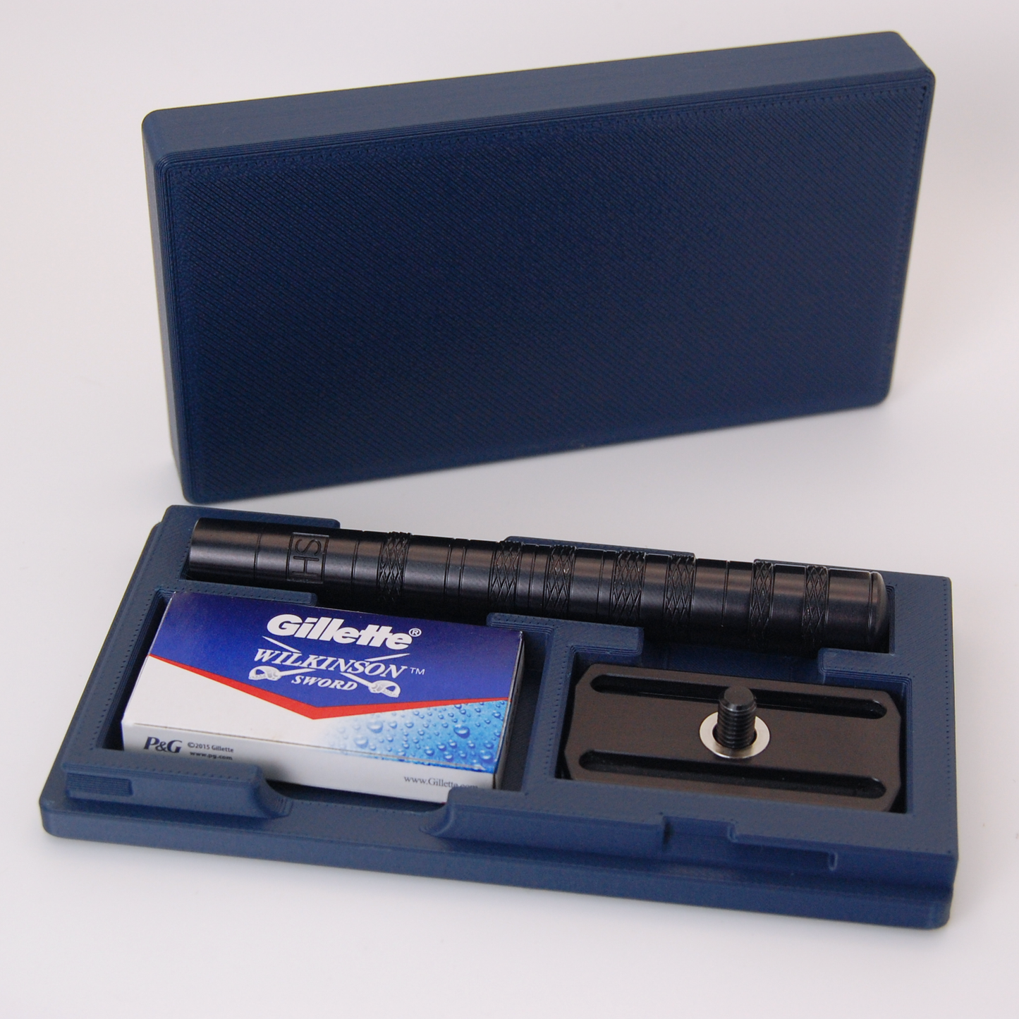 Henson case in navy blue on a white background.  Black Henson razor is stored inside with a blade tuck of Gillette Wilkinson Sword razor blades.
