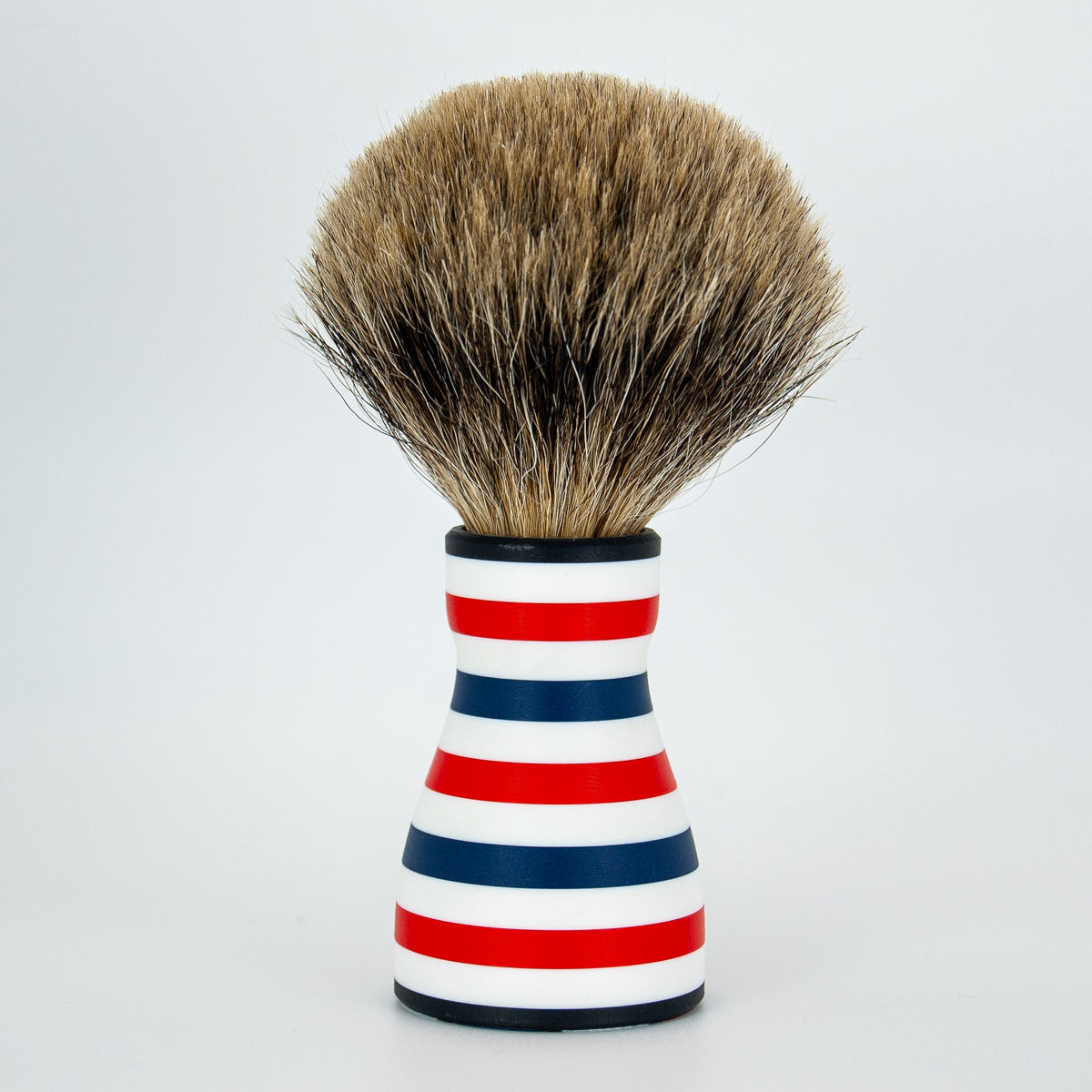 Rocket Nozzle shaving brush with 24mm finest badger bristle knot and red, white, and blue striped resin handle, upright on a white background