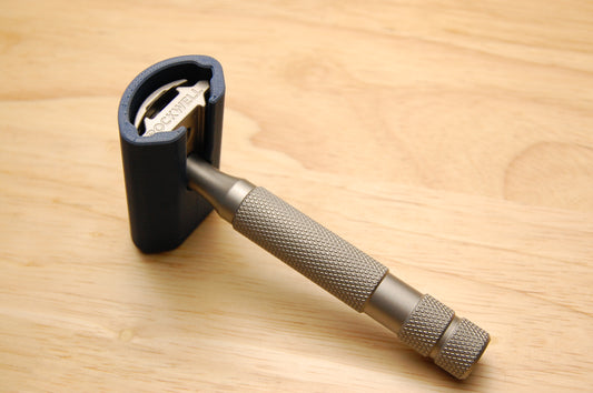 Rockwell safety razor with dark gray rubber travel cover on head, knurled stainless steel handle, on light wood surface