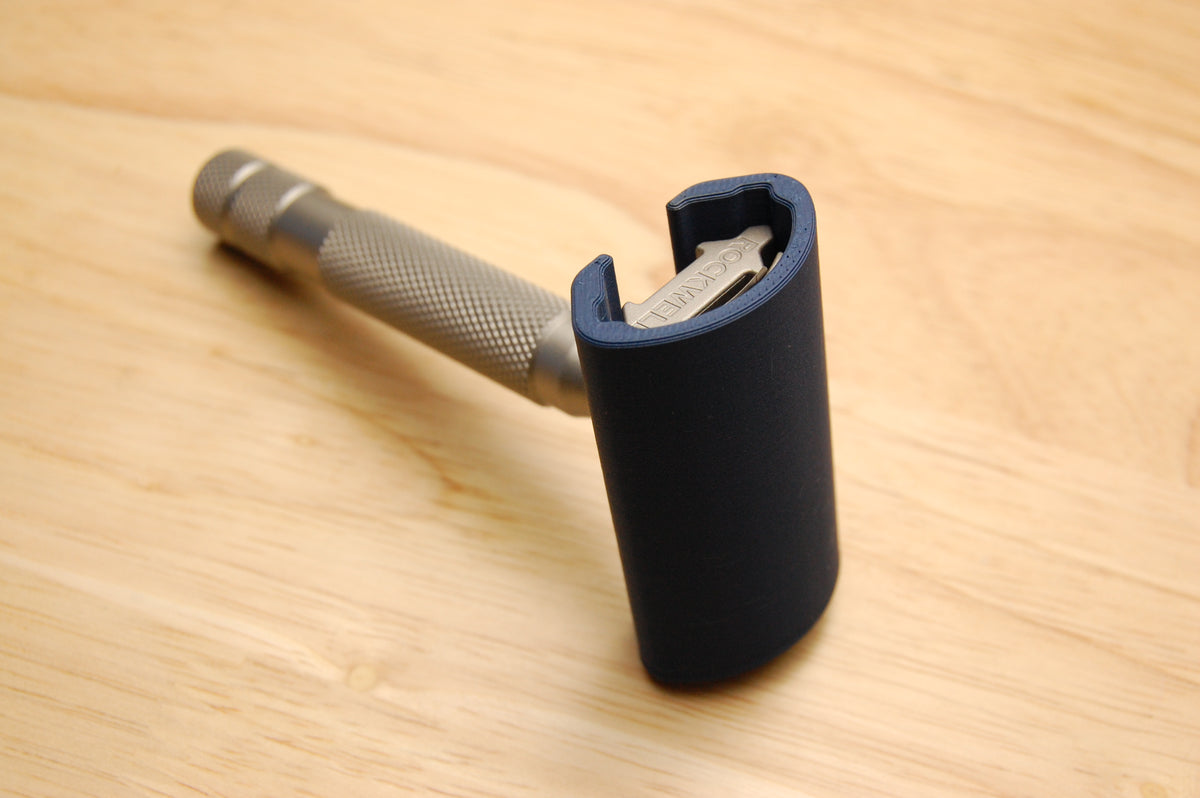 Rockwell safety razor with dark navy travel cover on blade head, knurled stainless steel handle, on light wood surface