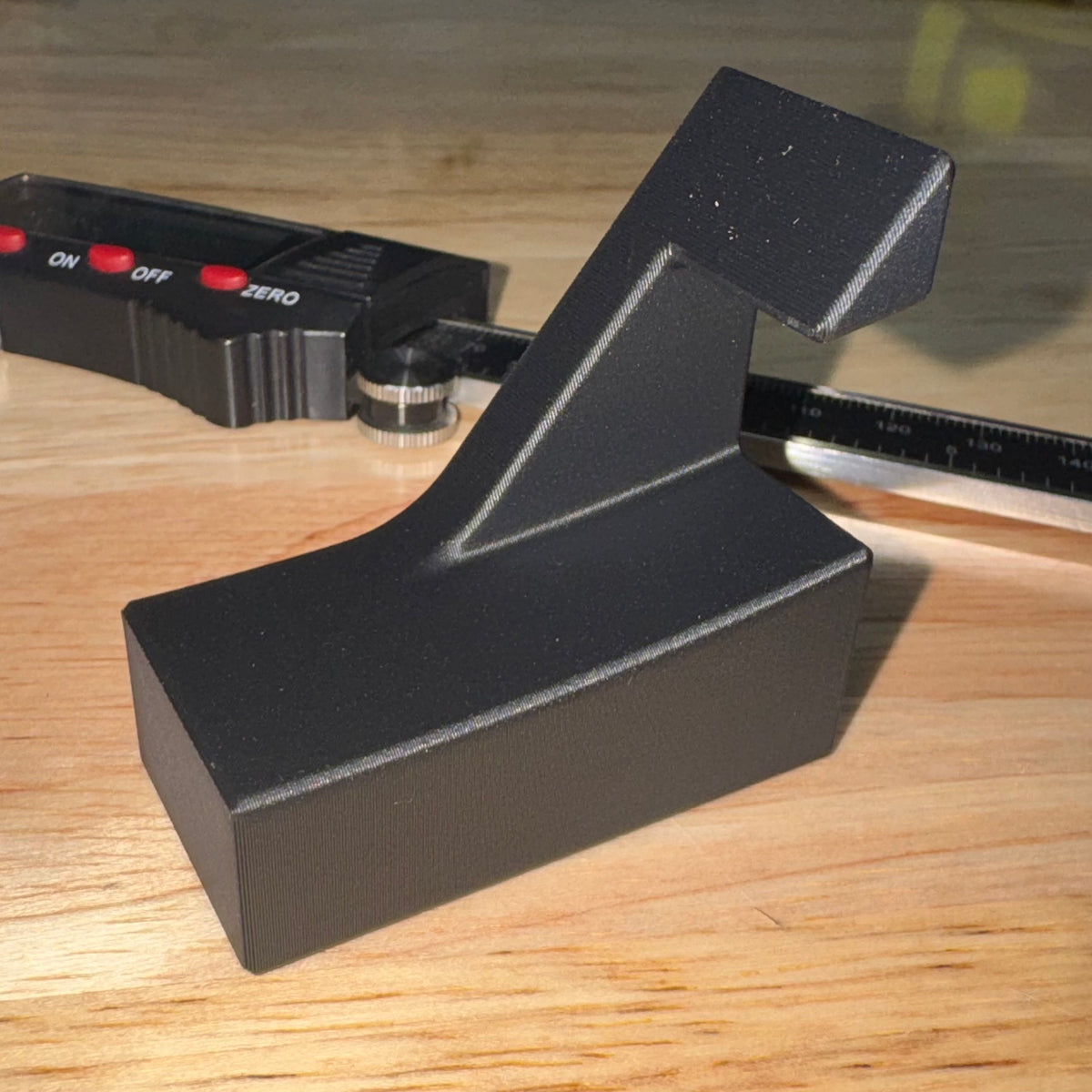 The Launch Pad black straight razor stand shown alone on a wood surface next to a digital caliper for scale