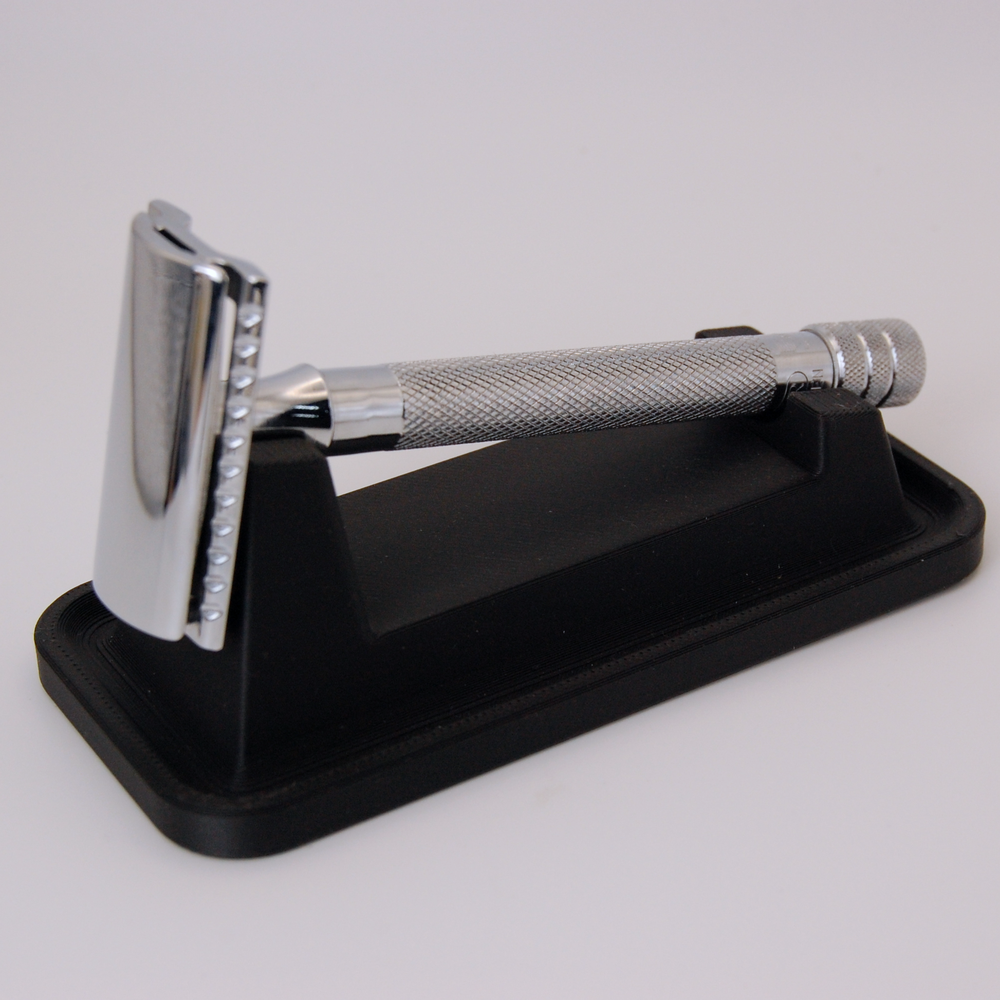 Universal razor stand with drip tray in black on a white background.  Pictured with a Merkur 23C razor.