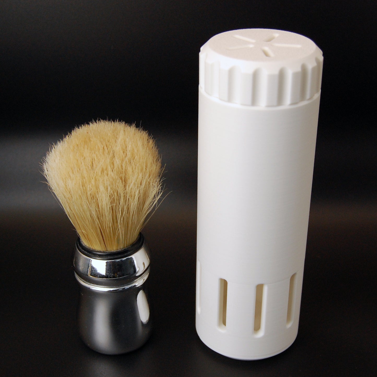 White vented shaving brush travel case on a black background with a brush sitting next to it.